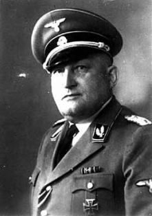 Richard Glücks.
A middle-aged man in a German SS uniform, with a cap on his head, remains serious.