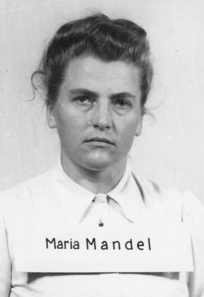 Process photo. A woman in a white blouse with collar and pinned back hair. She has a plaque with surname around her neck.
