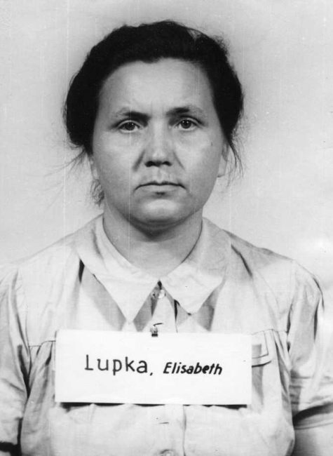 Prosses photo. Woman in a white blouse with collar and pinned back hair. She has a plaque with surname around her neck.