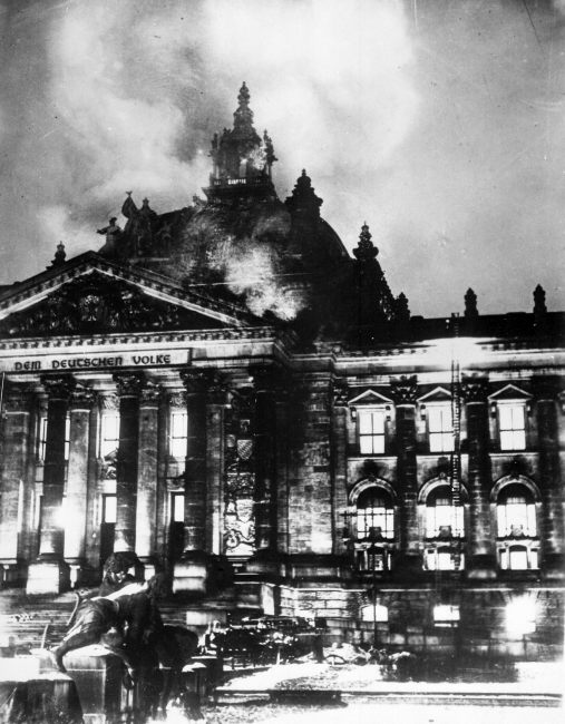 Budynek Reichstagu stio w płomieniach. Unosi się dym. 