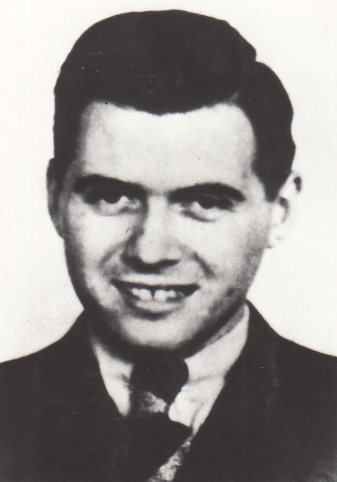 A photographic portrait of a smiling Dr. Mengele. Wearing a suit, a white shirt, and a tie.