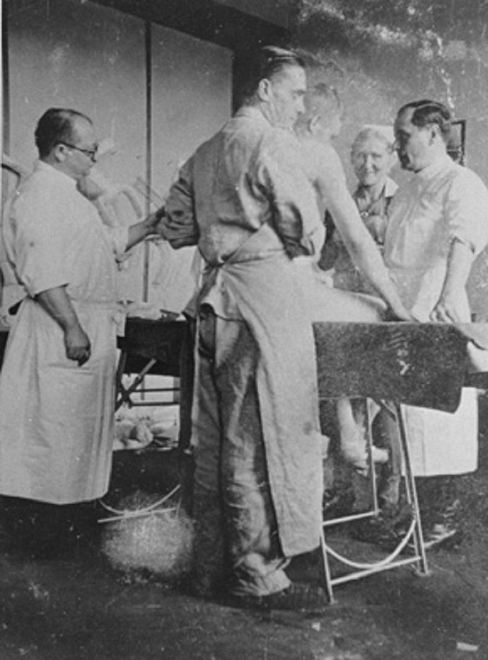 Three men in white coats standing around the operating table.  They are talking. A smiling nurse next to them. 