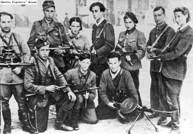 A group of young people, men and women, in uniforms and with rifles in their hands. Three men in the front row are kneeling, holding weapons.