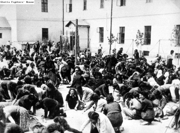 People kneeling and sitting on the ground in a fenced square.
