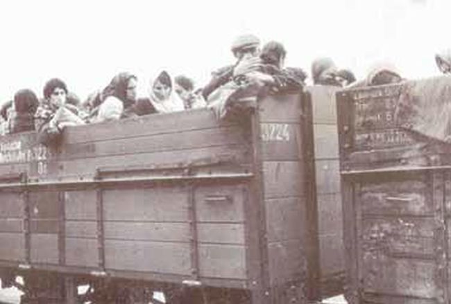 Transport ludzi w otwartych wagonach. Mężczyźni i kobiety w płaszczach i czapkach na głowach.