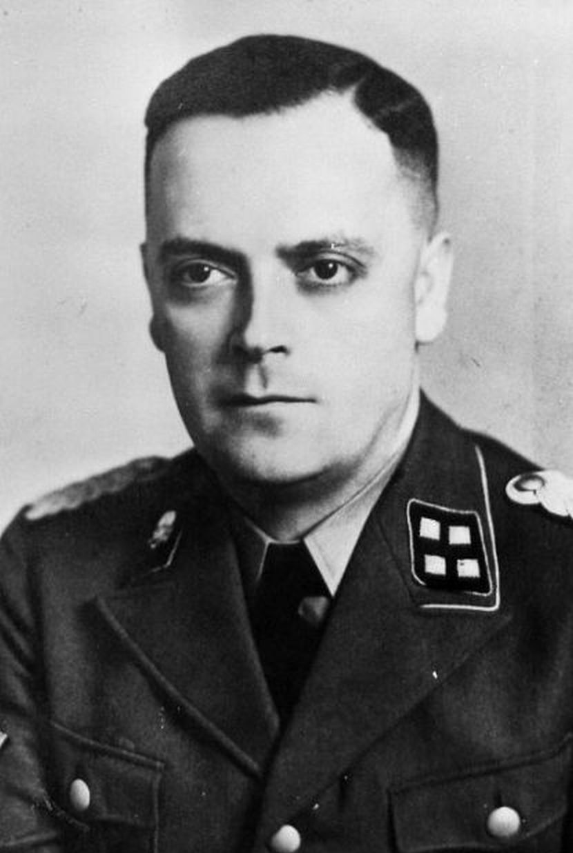 Middle-aged man in German SS uniform, keeping a serious expression. Gaze directed to the side of the camera. Dark hair, combed smoothly to the back.
