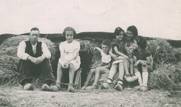 A family is sitting in front of a dugout covered with hay: a man, a woman and four children.
