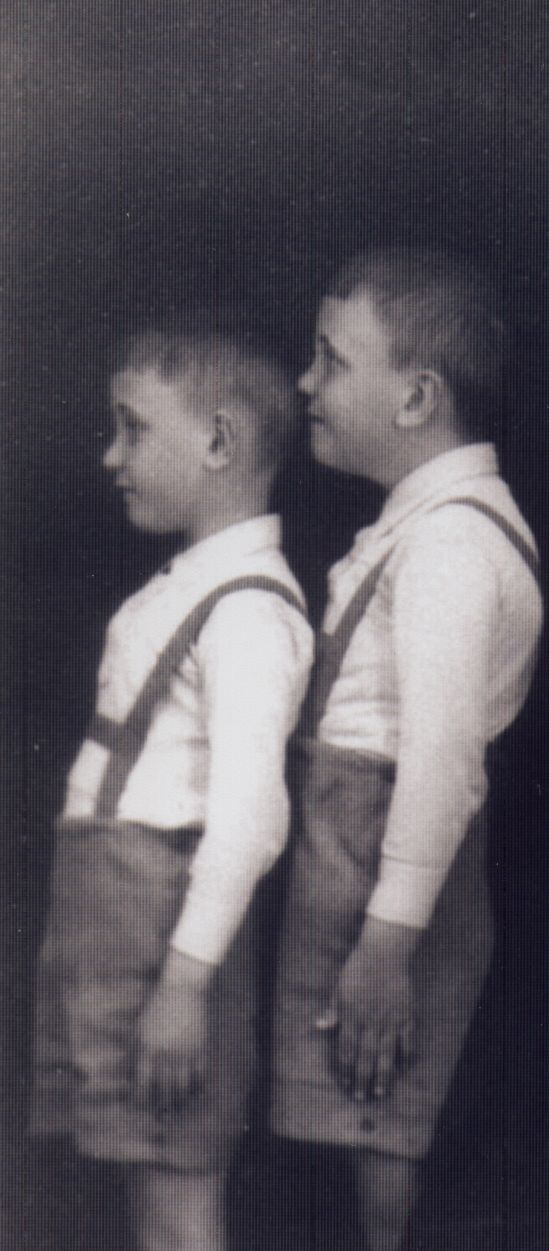 Otto Klein and his twin brother standing sideways to the camera. They are dressed in light long-sleeved shirts and dungarees.