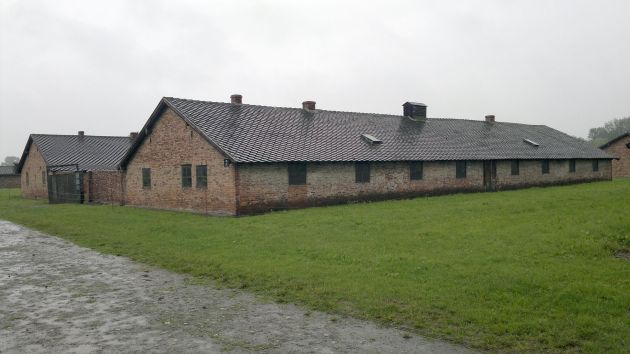 Two long single-storey brick-walled buildings. Small windows, sloped roof. Spacious lawn in the foreground.