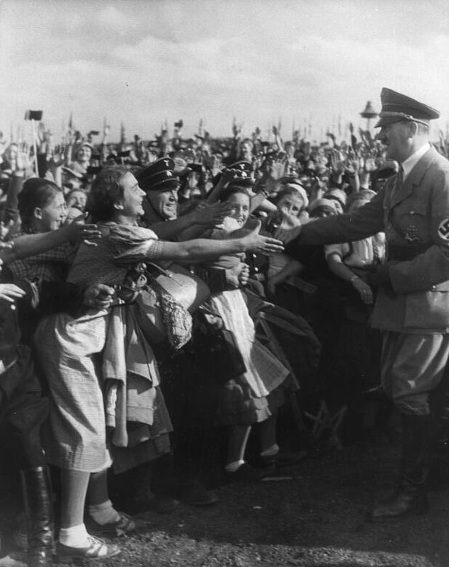 Adolf Hitler on the right greeting the crowd. Smiling women are greeting him back. One by one they want to shake his hand.
