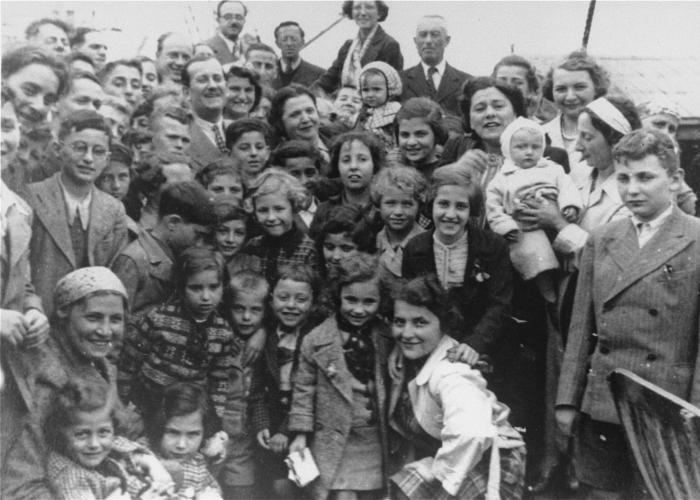 A crowd of children with their parents and carers posing for a photo. They are standing on the ship, smiling. Children of all ages, from infants to toddlers to teenagers.