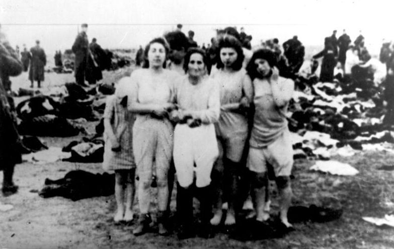 In the center of the photograph four women standing and a teenage girl hidden behind them. They are wearing only underwear. Behind them piles of clothes lie on the ground. Soldiers in the background. The moment before the execution.
