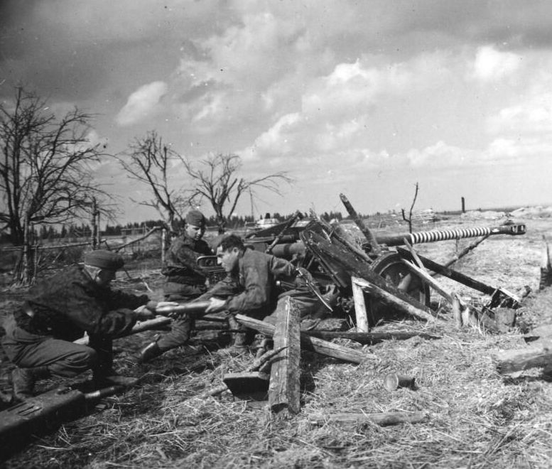 German soldiers next to a cannon. They are passing each other a shell to load. In the background leafless trees.