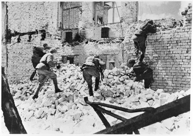 Soldiers in the midst of battle. Bent over, they are taking cover behind the ruins of a building. Bricks scattered around.