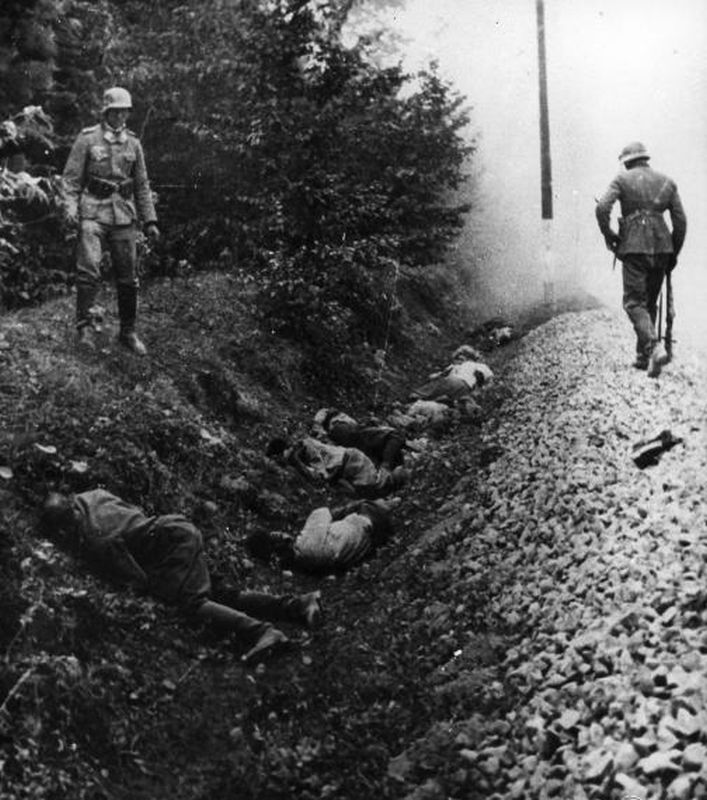 Bodies of murdered people lying in a ditch. A German soldier standing over them and looking on.