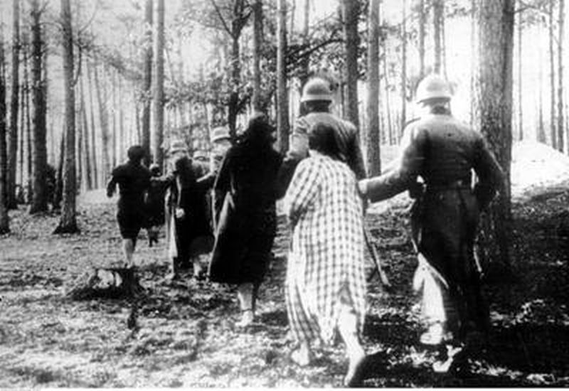 Forest. Women led arm in arm by German soldiers. Silhouettes turned away.