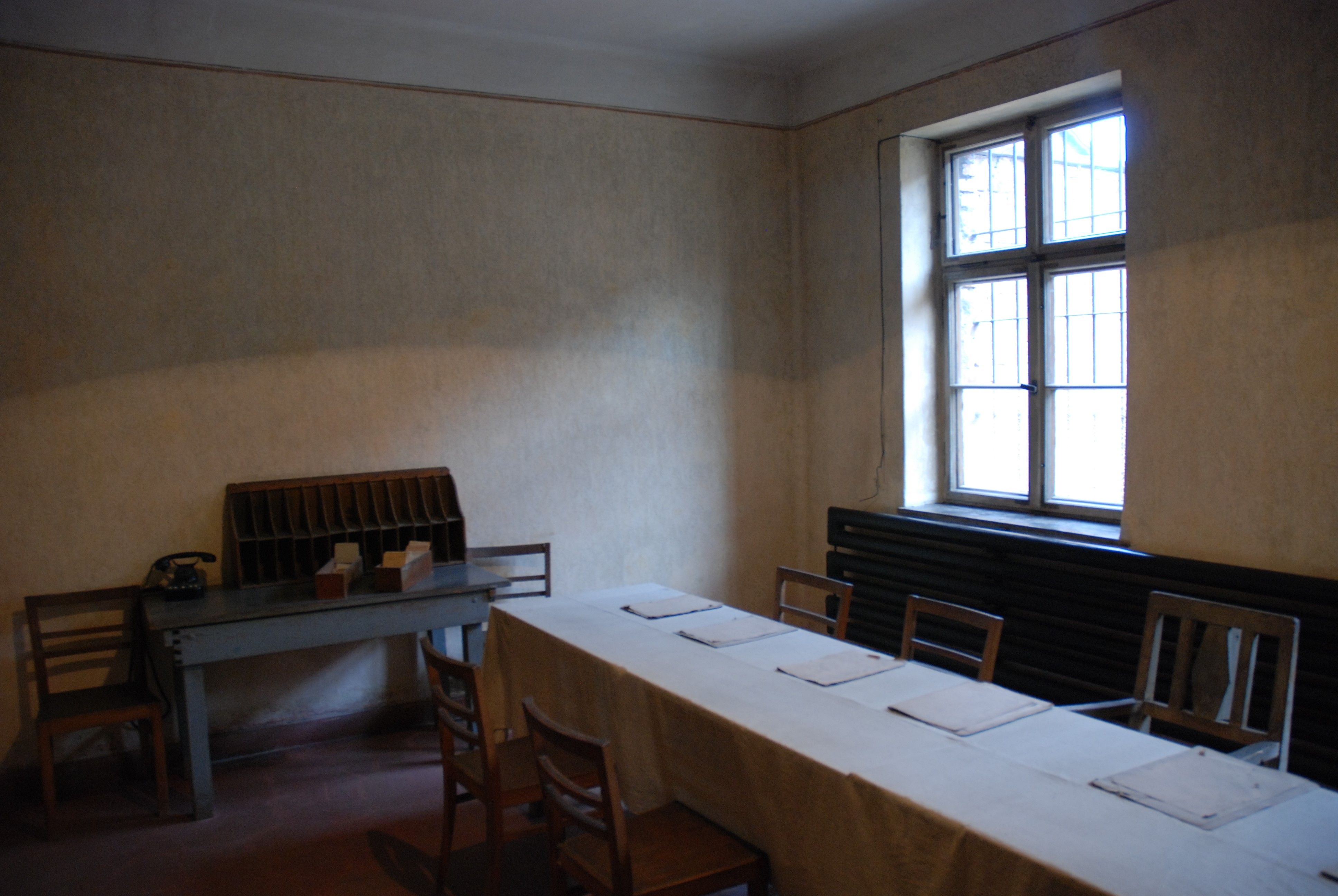 Interior of block 11 - summary courtroom – present-day state. On the right an oblong table on which copies of documents are laid out. On the left a desk and a chair. A window in the background.