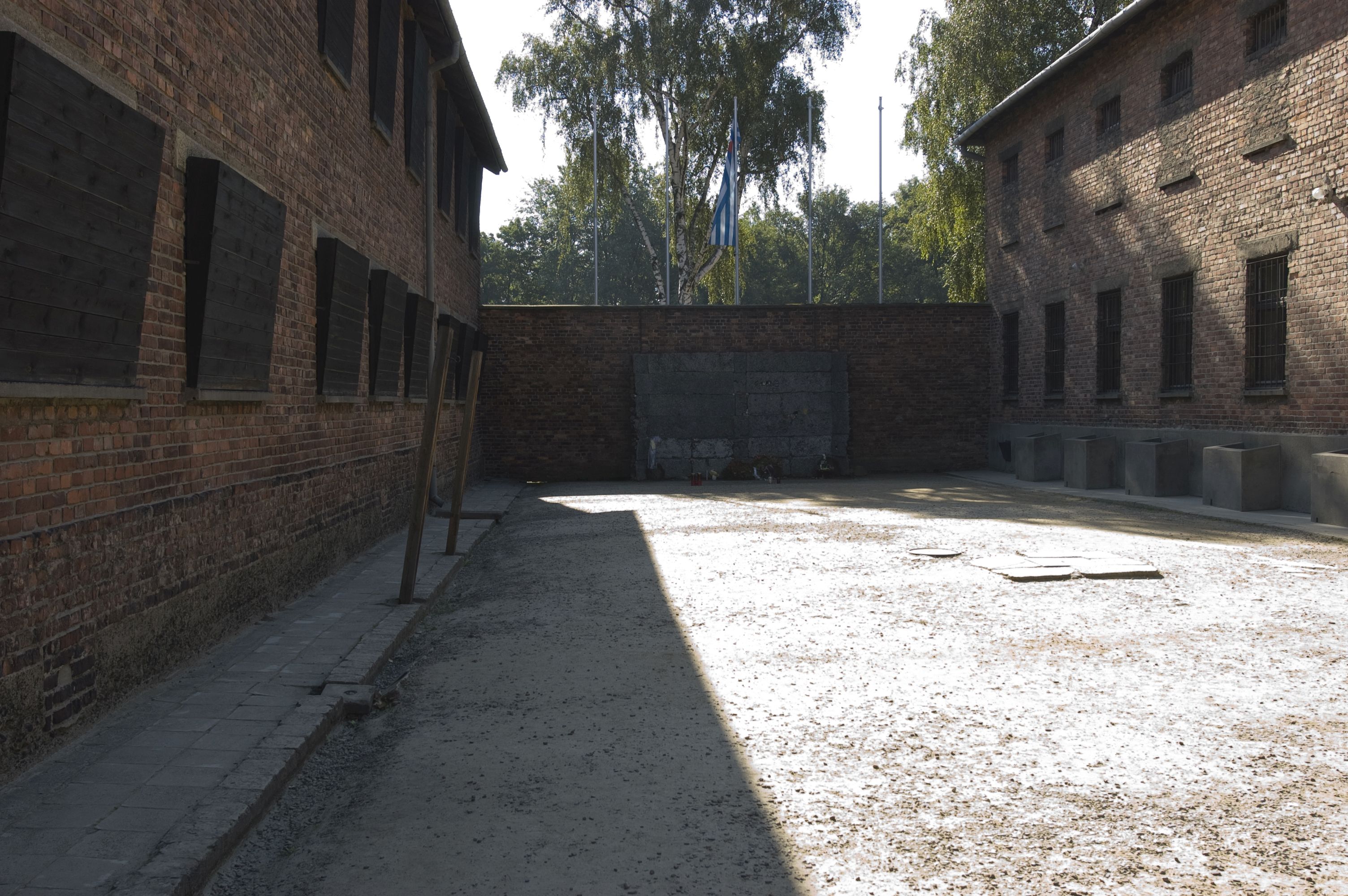 A wall between the two blocks 10 and 11. In front of it, in the courtyard of the blocks, a replica of the wall in front of which the prisoners were murdered. On the left are the shuttered windows of block 10, on the ground stakes are embedded - used for the punishment by the post.