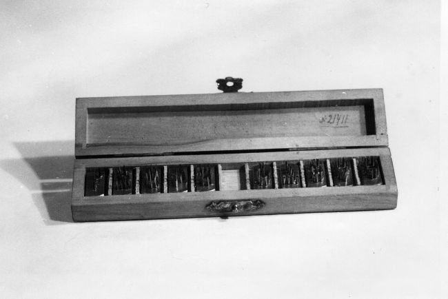 Opened wooden box with compartments. In the compartments metal fonts used for tattooing prisoners.