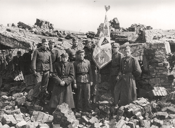 The guards of the Memorial Site standing on the ruins of the crematorium and gas chamber.  They are dressed in uniforms, one of them is holding a banner in his hand.