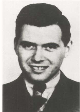 Photographic portrait of a smiling Dr Mengele. Dressed in a suit, a white shirt, a tie. Hair and eyes dark. Gaze directed towards the lens.