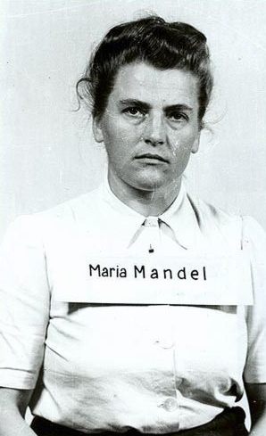 Marie Mandel
A middle-aged woman in a trial photo. Dressed in a white blouse with a collar. Dark hair, pinned up. Eyes directed towards the camera. She has a piece of paper with her name on her chest. Remains serious.