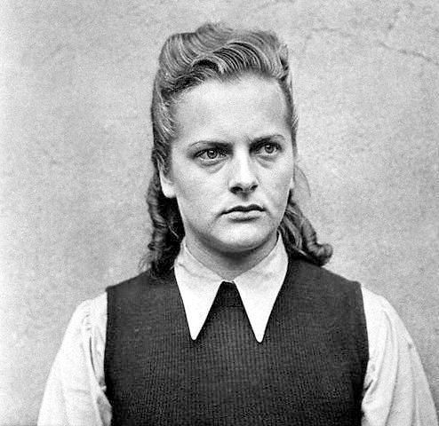 Irma Grese
A middle-aged woman wearing a blouse with a collar and a dark vest. Light hair, partially tied back. Glancing at the side of the camera. Remains serious.