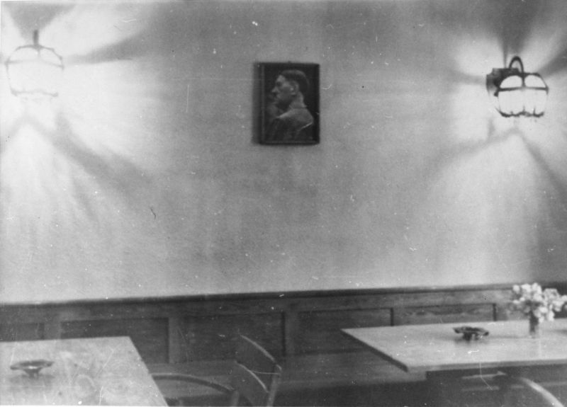 One of the offices at the SS Institute of Hygiene. Tables, chairs, ashtrays on the tables, and a vase with flowers on one of them. A portrait of Hitler hanging on the wall.