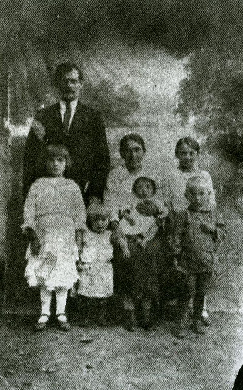 A studio portrait of the Antonina and Antoni Niemirek family. Antoni is dressed in a suit, standing. Four children dressed in festive clothes are also standing next to him. Antonina is sitting on a chair, holding her youngest, fifth child on her lap.